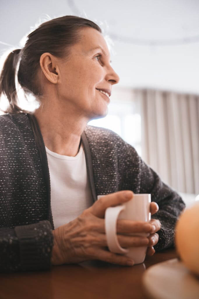 Senior woman holding a mug, smiling and enjoying a warm drink indoors.